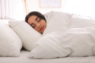 Photo of Young woman covered with warm white blanket sleeping in bed at home