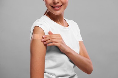 Photo of Woman with sticking plaster on arm after vaccination against light grey background, closeup