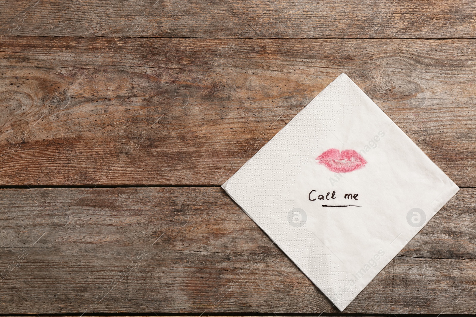 Photo of Paper napkin with lipstick mark and words CALL ME on wooden background, top view. Space for text