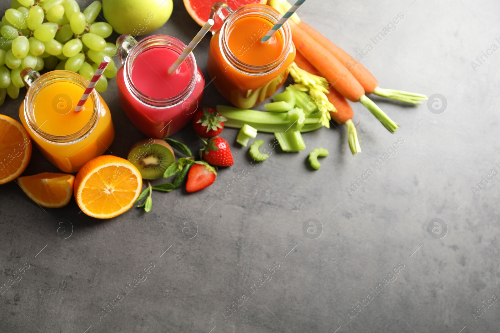 Photo of Different juices in mason jars and fresh ingredients on grey background, top view. Space for text