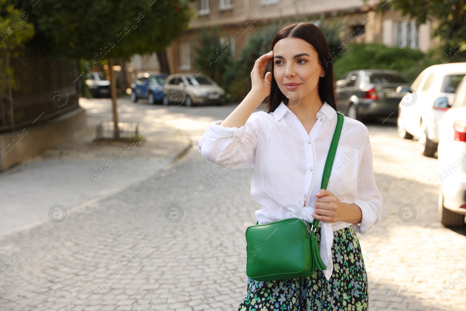 Photo of Beautiful young woman with stylish bag on city street, space for text