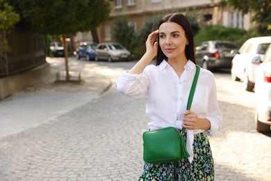 Photo of Beautiful young woman with stylish bag on city street, space for text