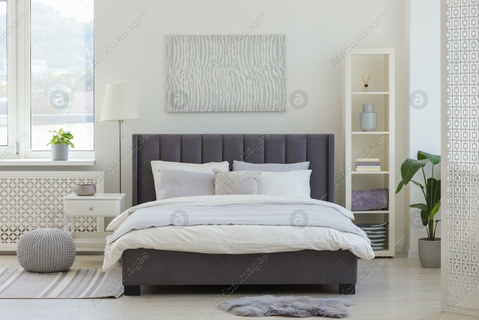 Photo of Stylish light bedroom interior with large comfortable bed, shelving unit and bedside table