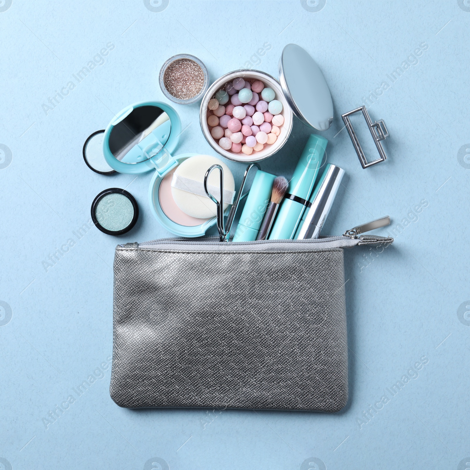 Photo of Cosmetic bag with makeup products and beauty accessories on light blue background, flat lay