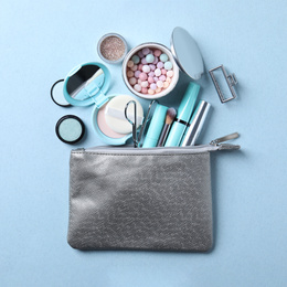 Cosmetic bag with makeup products and beauty accessories on light blue background, flat lay