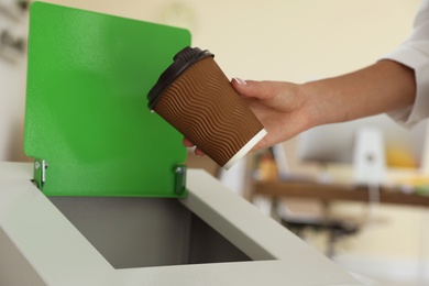 Woman throwing coffee cup into recycling bin at office, closeup