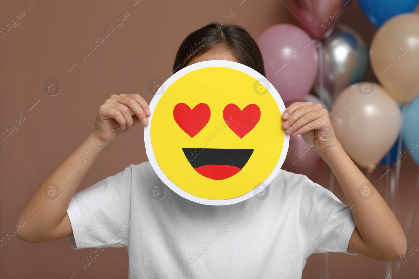 Photo of Little girl covering face with heart eyes emoji in decorated room