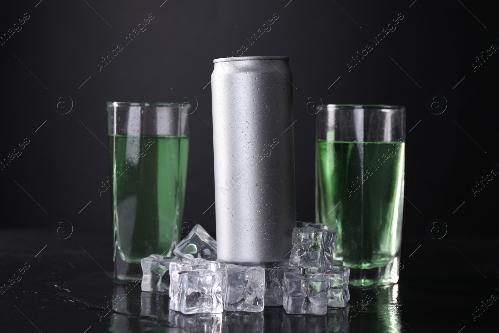 Photo of Energy drink in glasses, aluminium can and ice cubes on black table