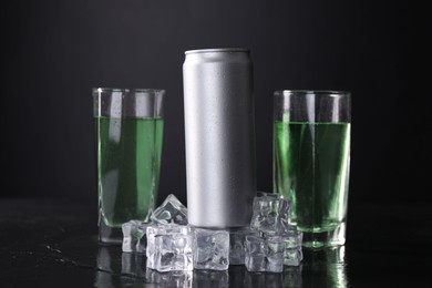 Photo of Energy drink in glasses, aluminium can and ice cubes on black table