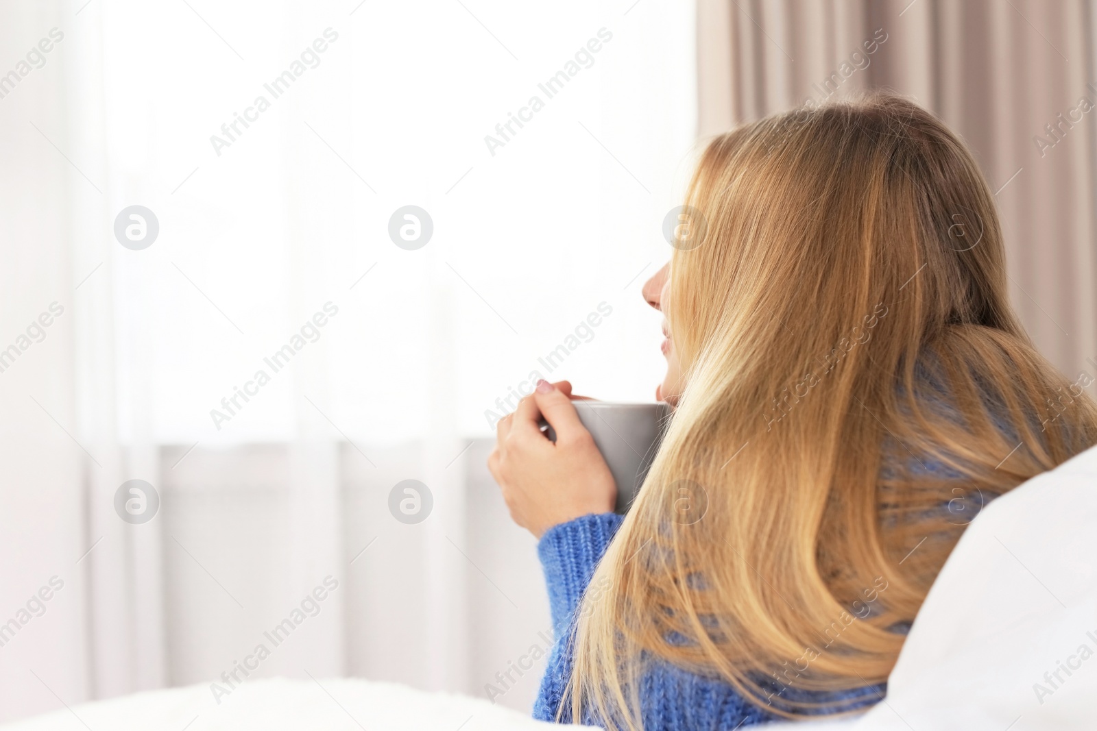 Photo of Beautiful young woman lying with cup in bed at home. Winter atmosphere