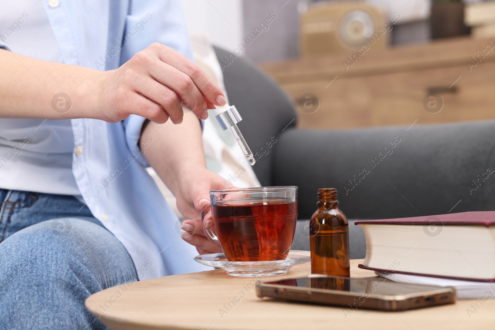 Photo of Woman dripping food supplement into cup of tea at wooden table indoors, closeup