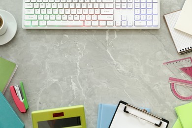 Frame of modern keyboard with RGB lighting and stationery on grey table, flat lay. Space for text