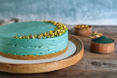 Photo of Delicious homemade spirulina cheesecake decorated with pistachios on wooden table. Space for text