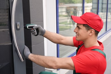 Photo of Handyman with screw gun repairing door lock outdoors