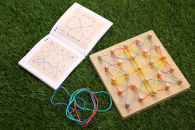 Photo of Wooden geoboard with rubber bands and activity book on artificial grass. Educational toy for motor skills development