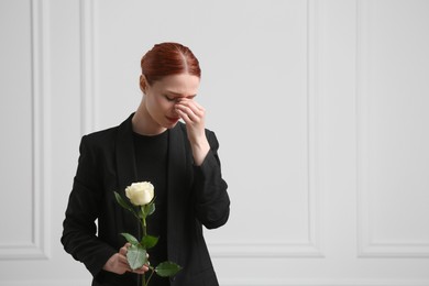 Photo of Sad woman with rose flower mourning near white wall, space for text. Funeral ceremony