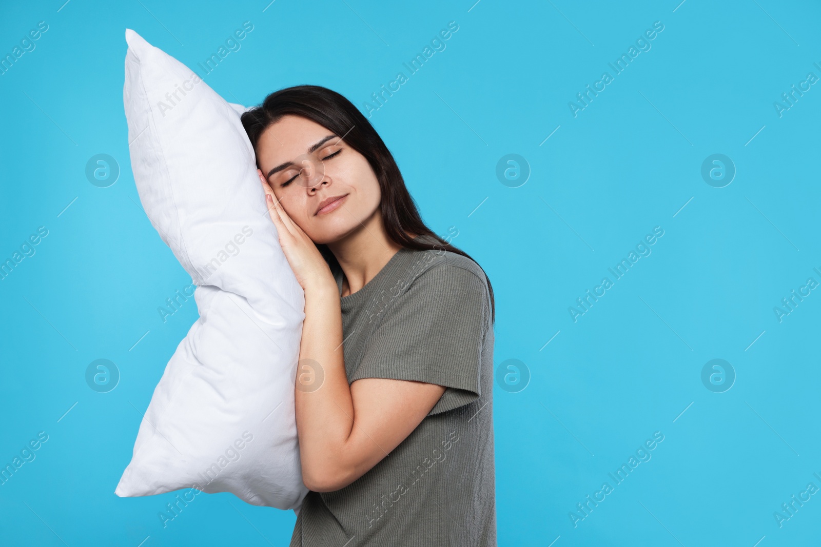 Photo of Sleepy young woman with soft pillow on light blue background, space for text