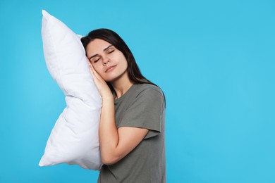 Sleepy young woman with soft pillow on light blue background, space for text