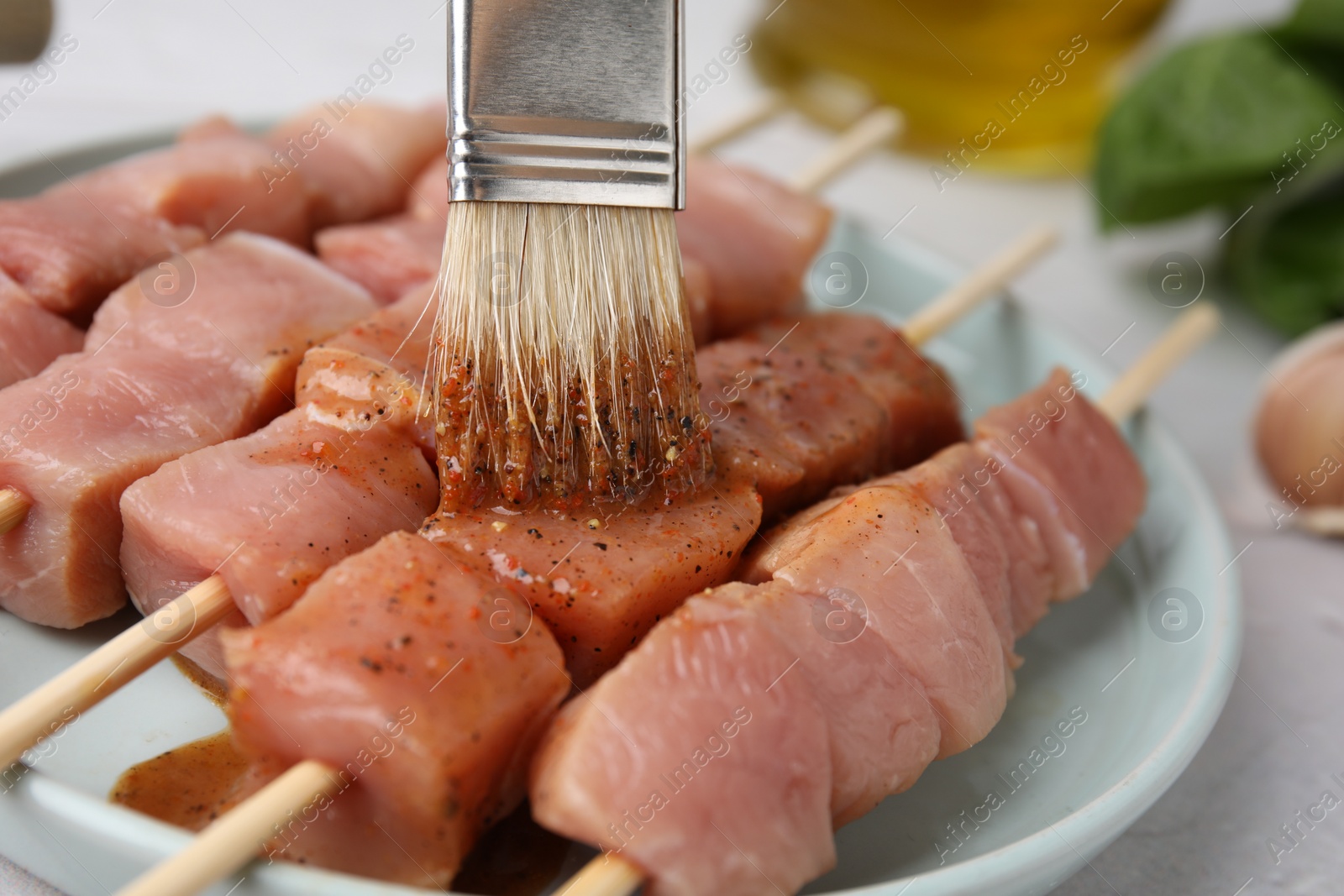 Photo of Spreading marinade onto raw meat with basting brush on light table, closeup