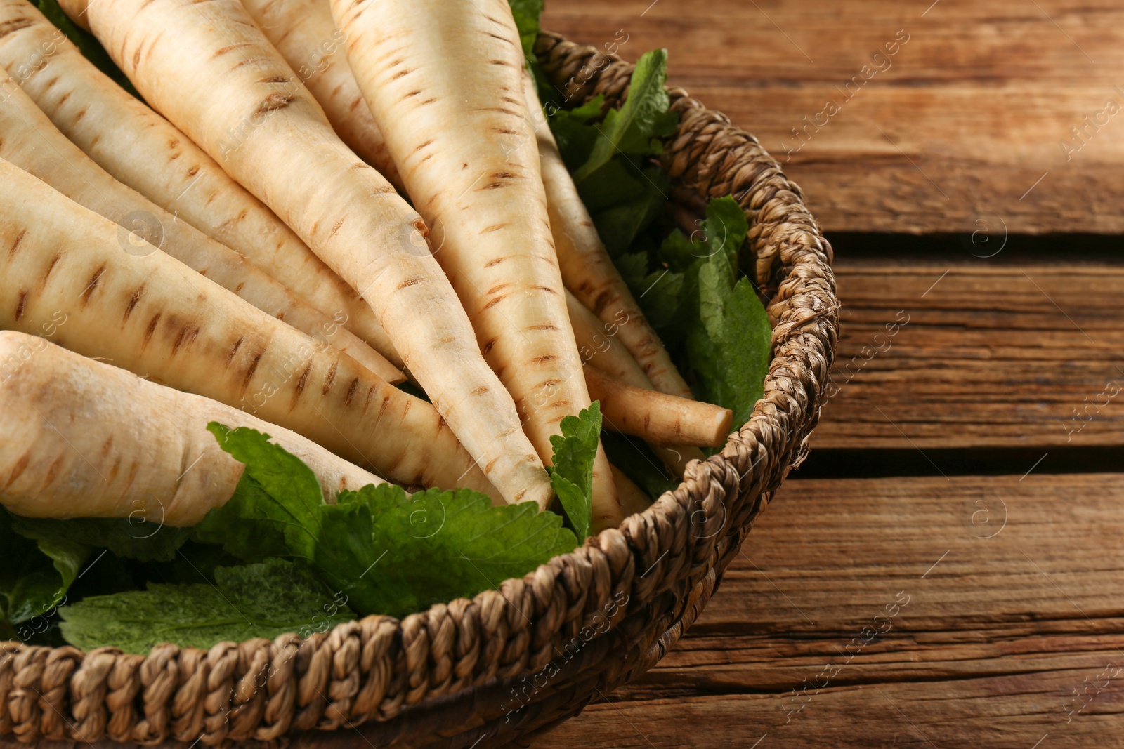 Photo of Fresh ripe parsnips in wicker basket on wooden table, closeup. Space for text