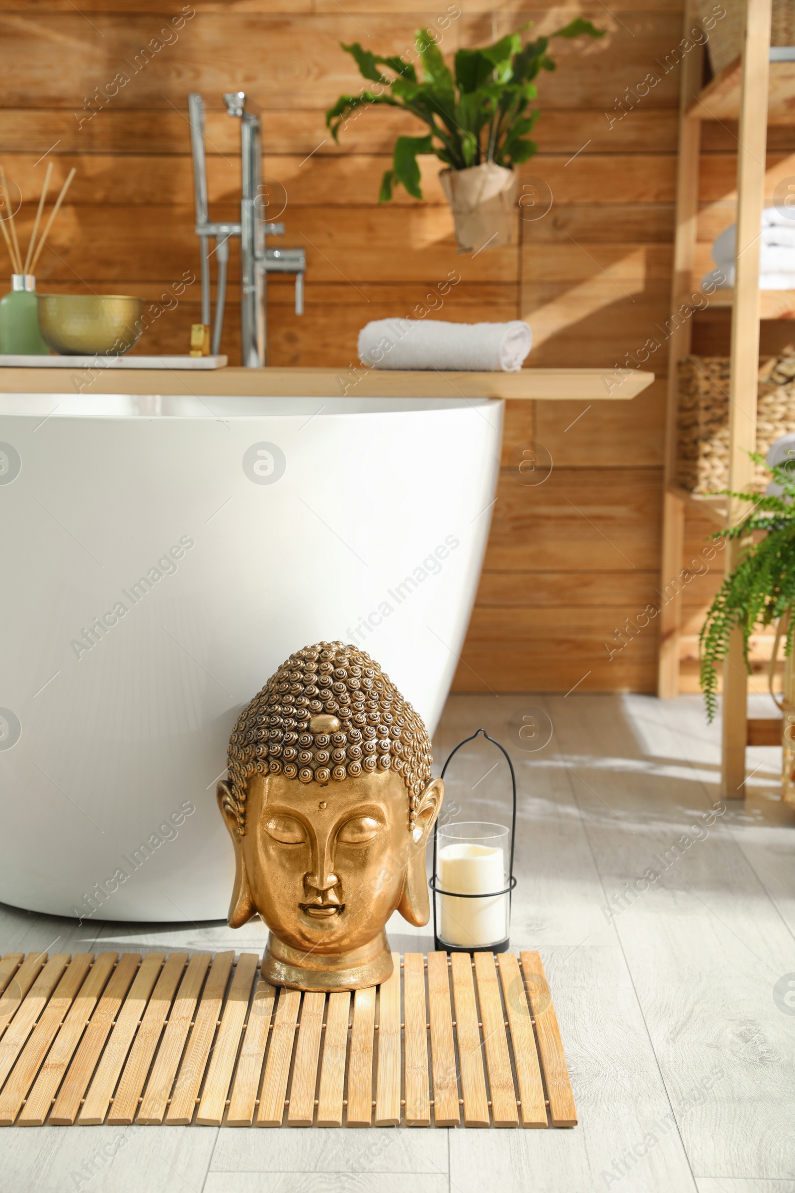 Photo of Golden Buddha sculpture and candle near white tub in bathroom. Interior design