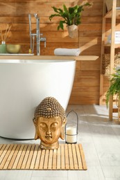 Golden Buddha sculpture and candle near white tub in bathroom. Interior design