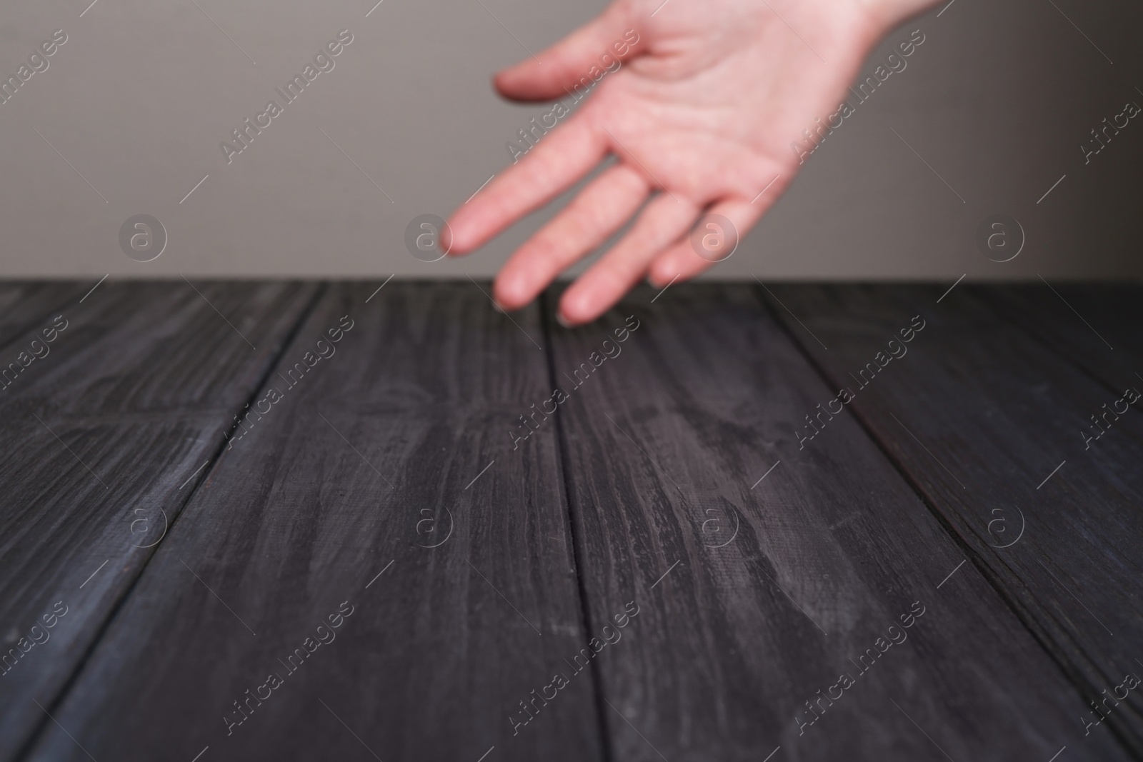 Photo of Woman holding hand above black wooden table, selective focus. Space for text