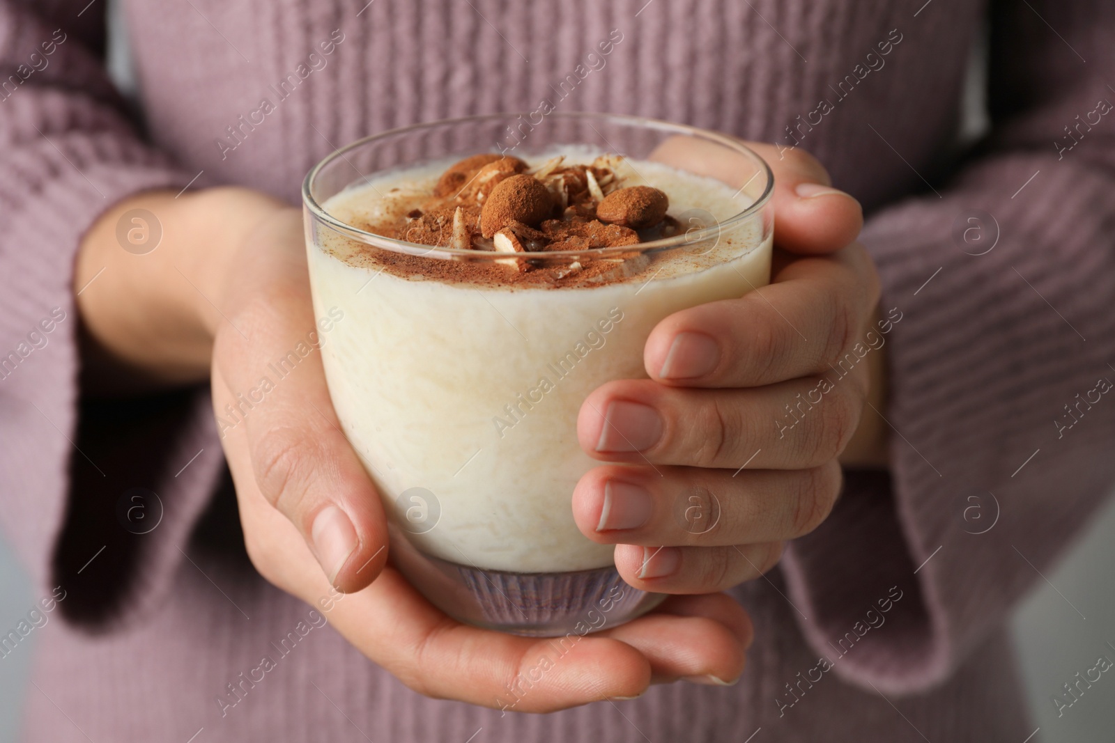 Photo of Woman holding glass of delicious rice pudding with cinnamon and almonds, closeup