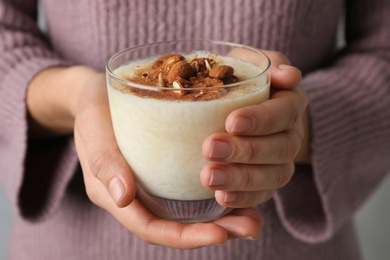 Woman holding glass of delicious rice pudding with cinnamon and almonds, closeup