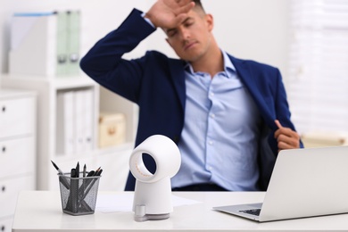 Photo of Man suffering from heat at workplace, focus on fan