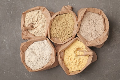 Paper bags with different types of flour on gray background