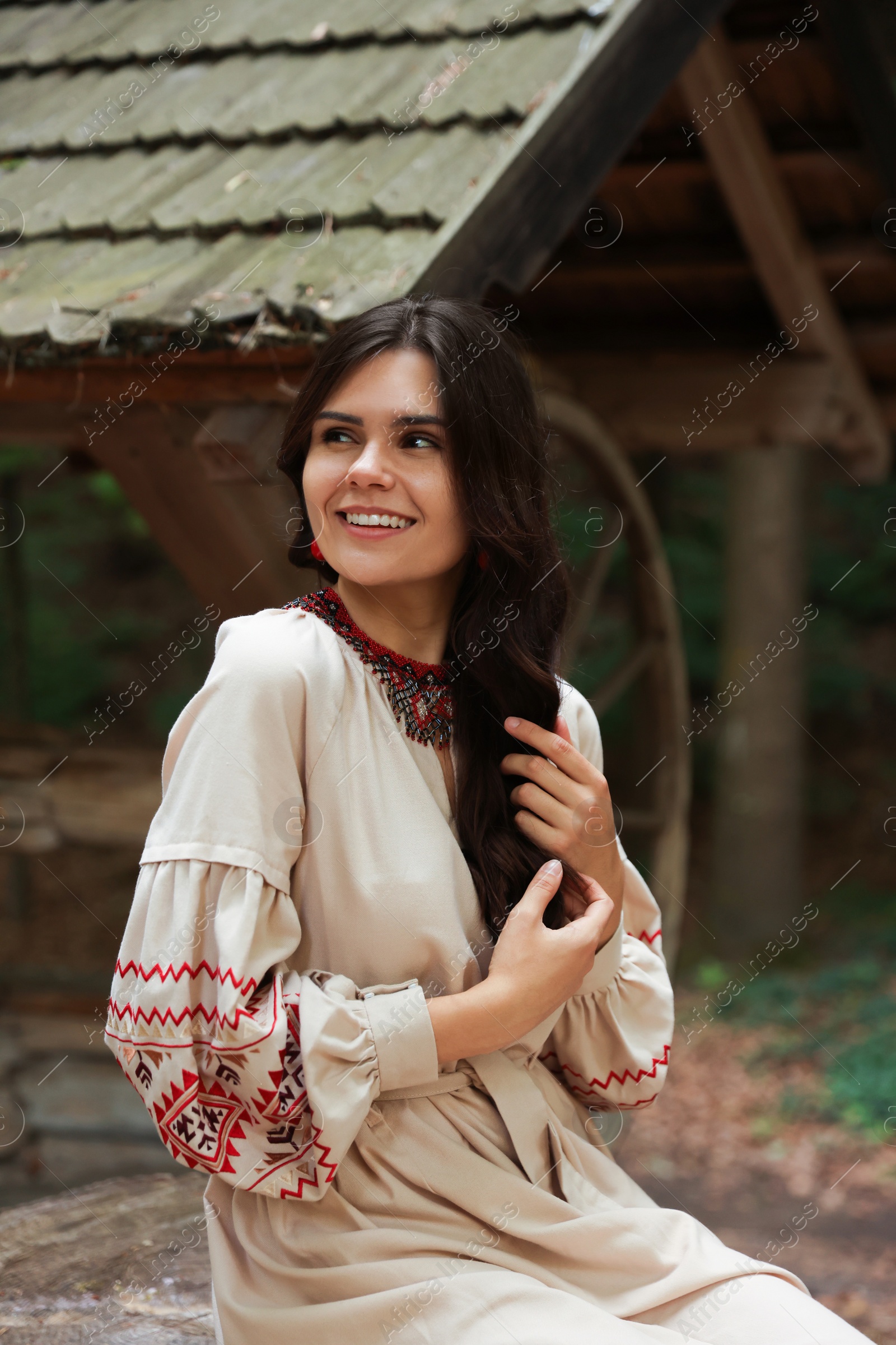 Photo of Beautiful woman wearing embroidered dress sitting near old wooden well in countryside. Ukrainian national clothes