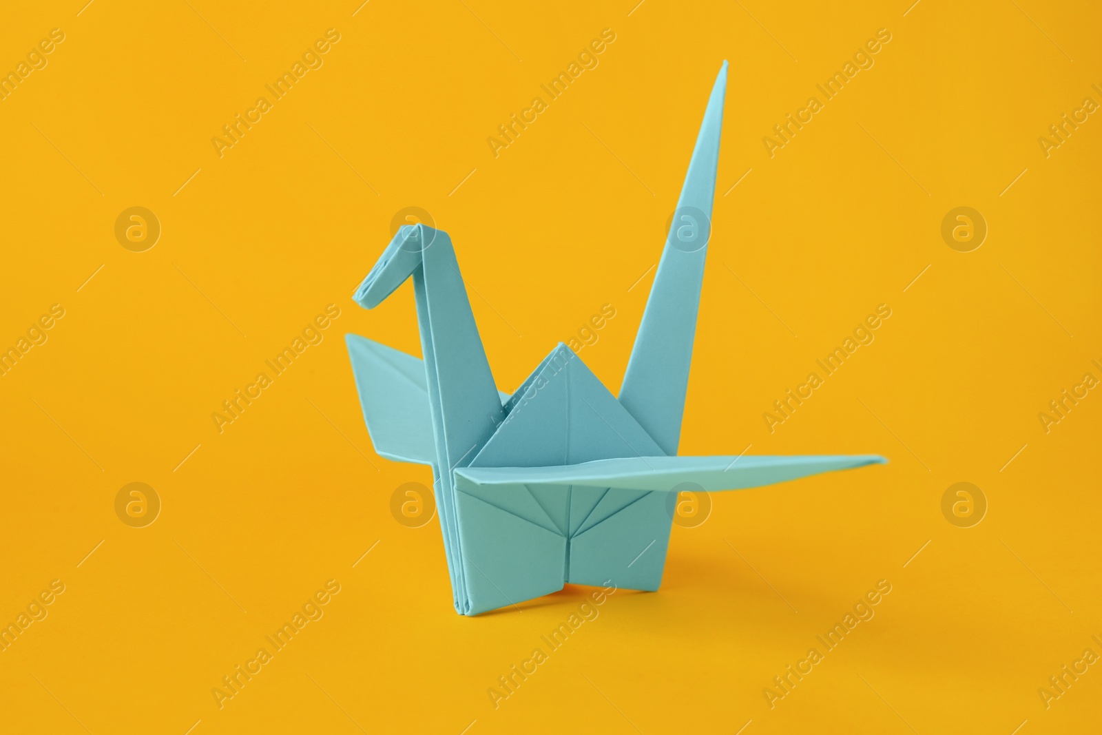 Photo of Origami art. Beautiful light blue paper crane on orange background