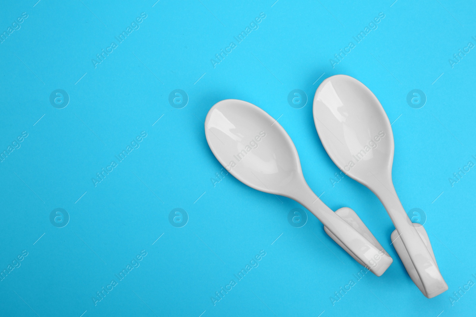 Photo of Clean empty ceramic appetizer spoons on blue background, top view. Space for text