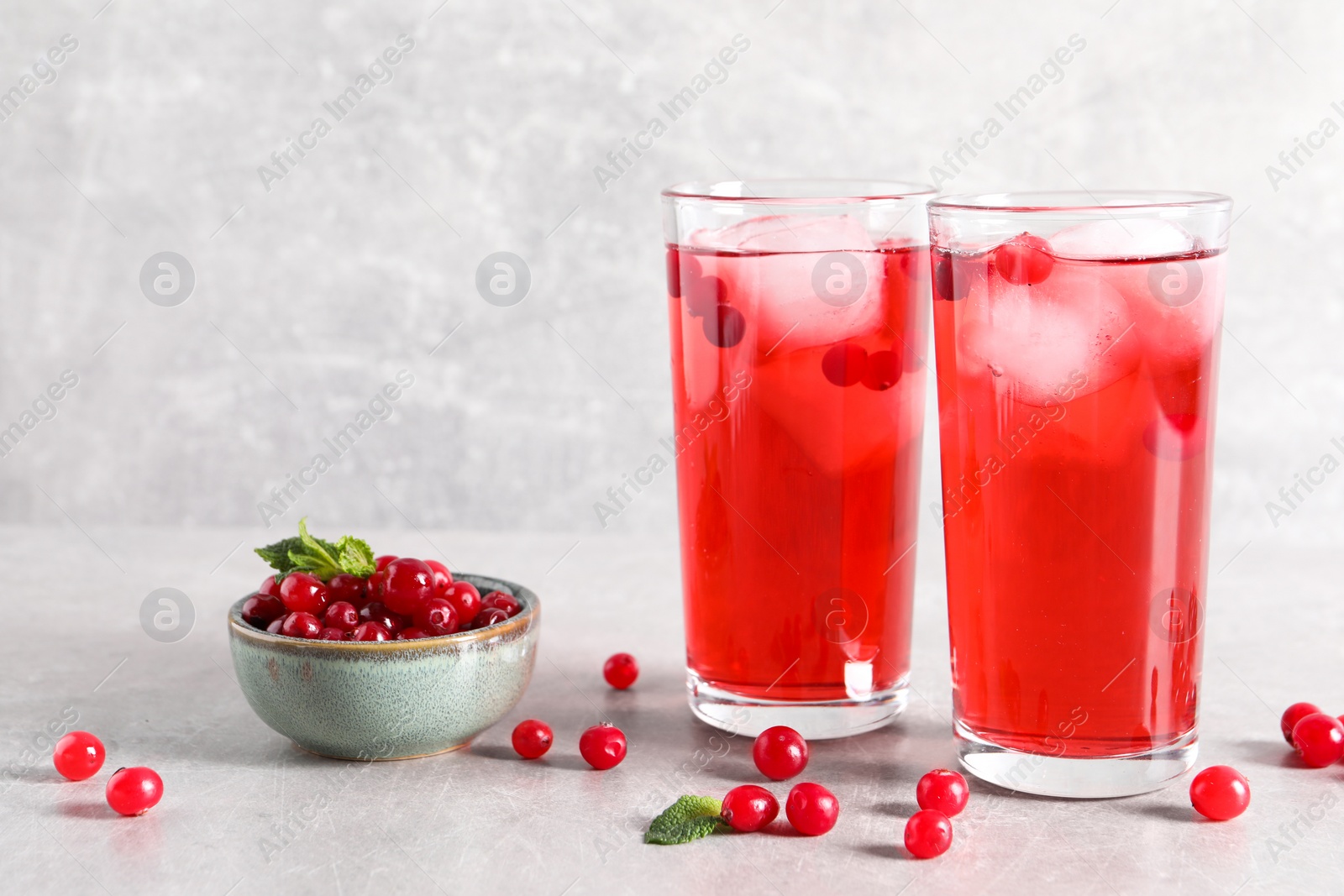 Photo of Tasty cranberry juice with ice cubes in glasses and fresh berries on light grey table