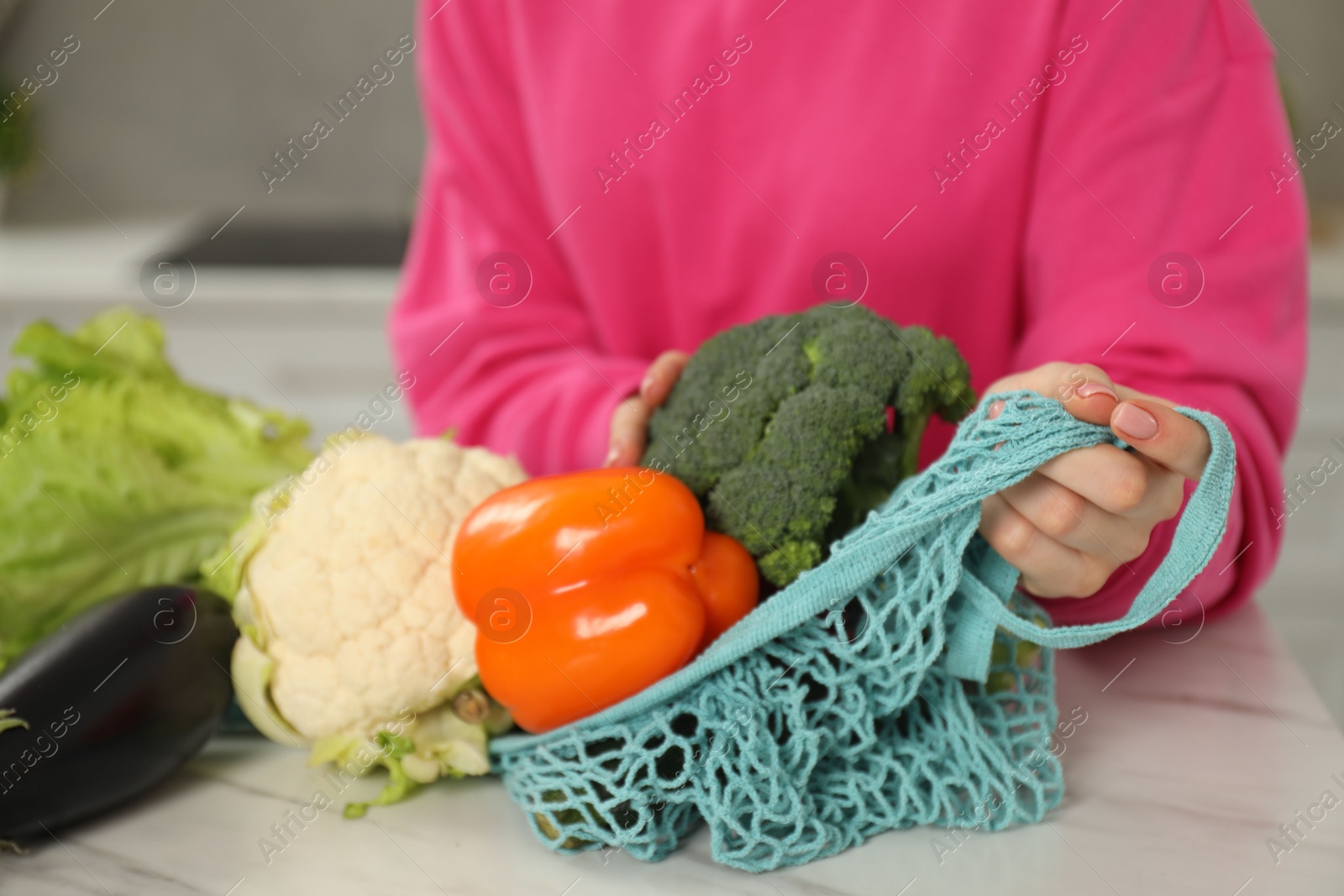 Photo of Woman with string bag of fresh vegetables at light marble table, closeup