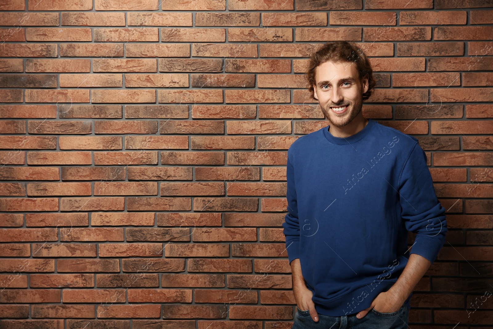 Photo of Handsome young man in warm sweater near brick wall. Space for text