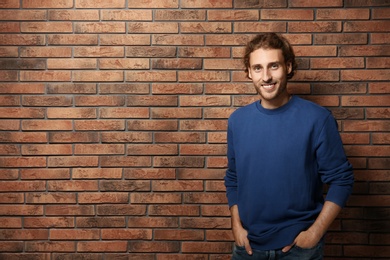 Photo of Handsome young man in warm sweater near brick wall. Space for text