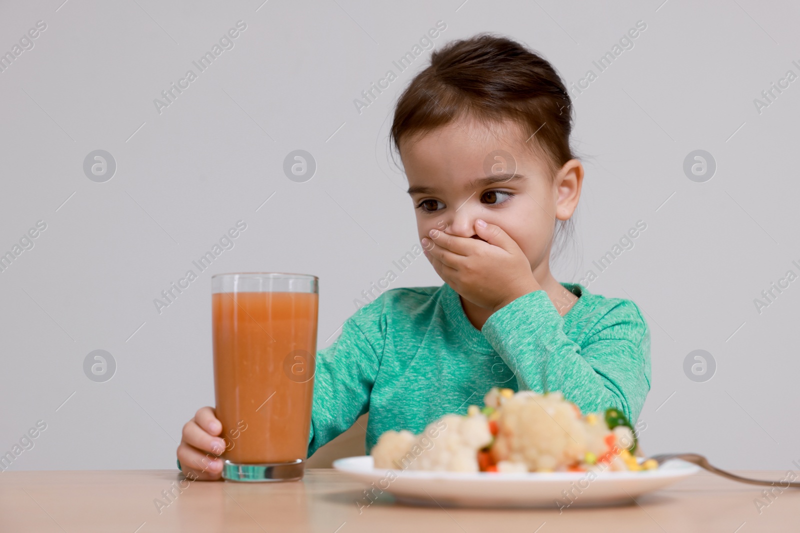 Photo of Cute little girl covering mouth and refusing to drink juice at table on grey background