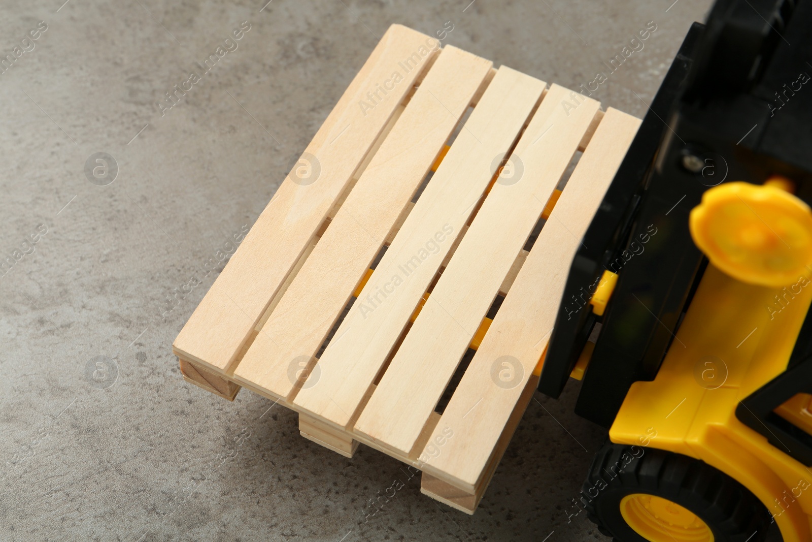 Photo of Toy forklift with wooden pallet on light grey table, closeup