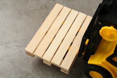 Photo of Toy forklift with wooden pallet on light grey table, closeup