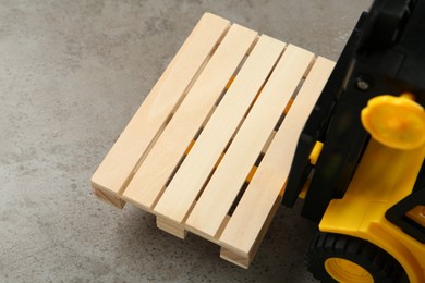 Toy forklift with wooden pallet on light grey table, closeup