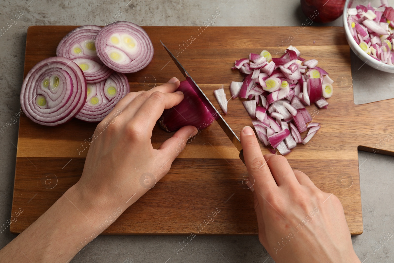 Photo of Woman cutting red onion on wooden board at grey table, above view