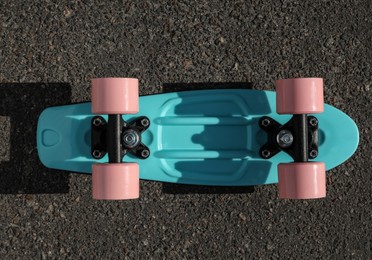 Photo of Modern light blue skateboard with pink wheels on asphalt road outdoors, top view