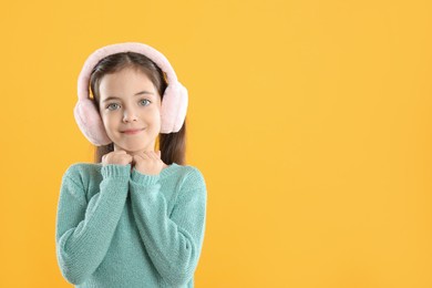 Photo of Cute girl wearing stylish earmuffs on yellow background. Space for text