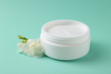 Moisturizing cream in open jar and freesia flower on turquoise background. Body care product