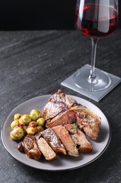 Delicious fried beef meat, vegetables and glass of wine on black table