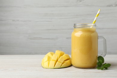 Mason jar with delicious fruit smoothie and fresh mango on white wooden table. Space for text