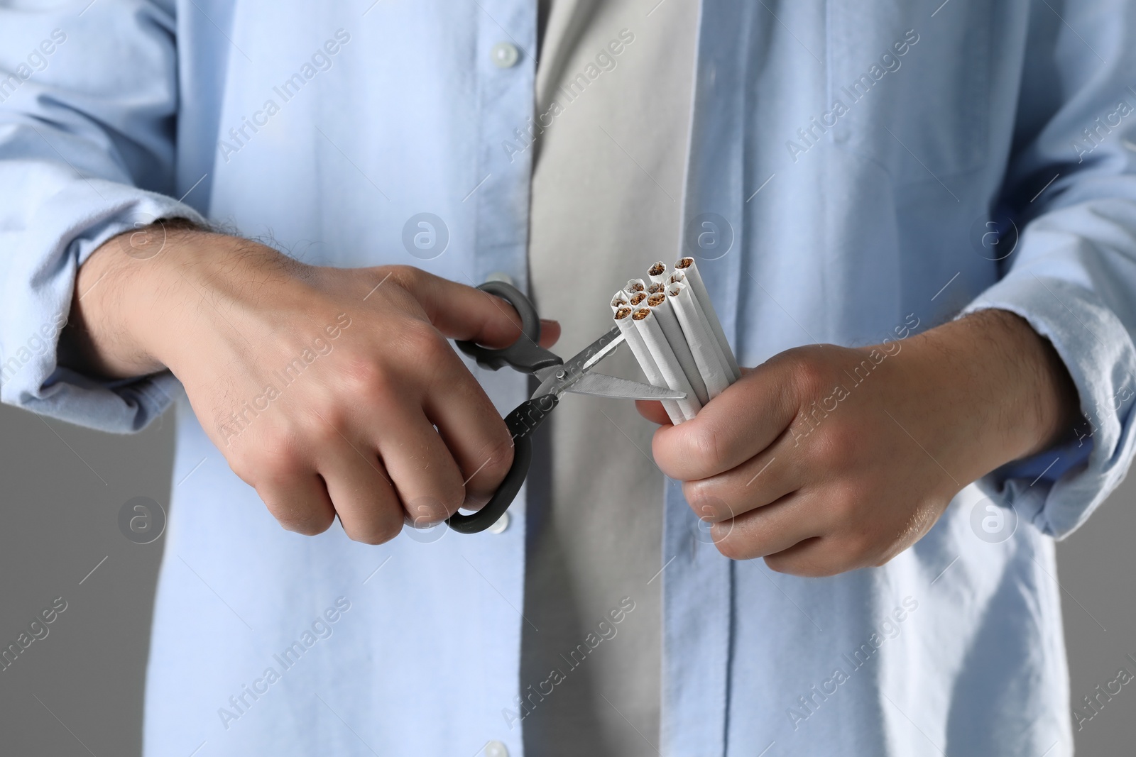 Photo of Stop smoking concept. Man cutting cigarettes on gray background, closeup