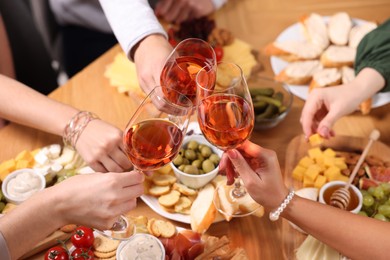 Photo of People clinking glasses with rose wine at wooden table, above view